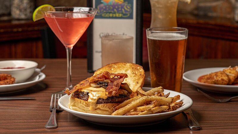 Cheeseburger topped with mushrooms and bacon with a cocktail and a pint of beer